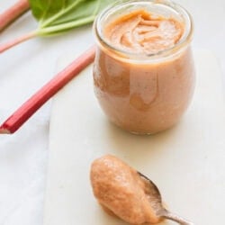 A spoon and a jar of rhubarb curd next to a rhubarb