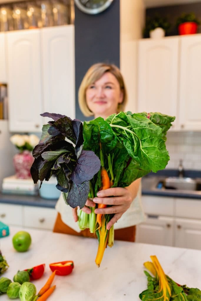 abra pappa holding a big bunch of greens in her kitchen