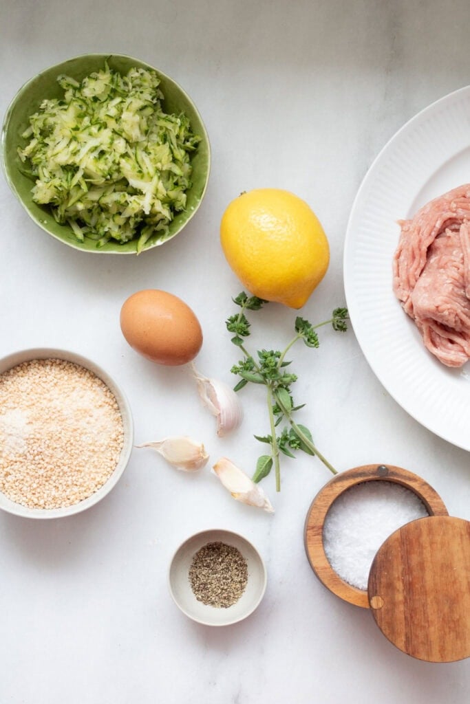Ingredients for turkey zucchini meatballs in small bowls on white background