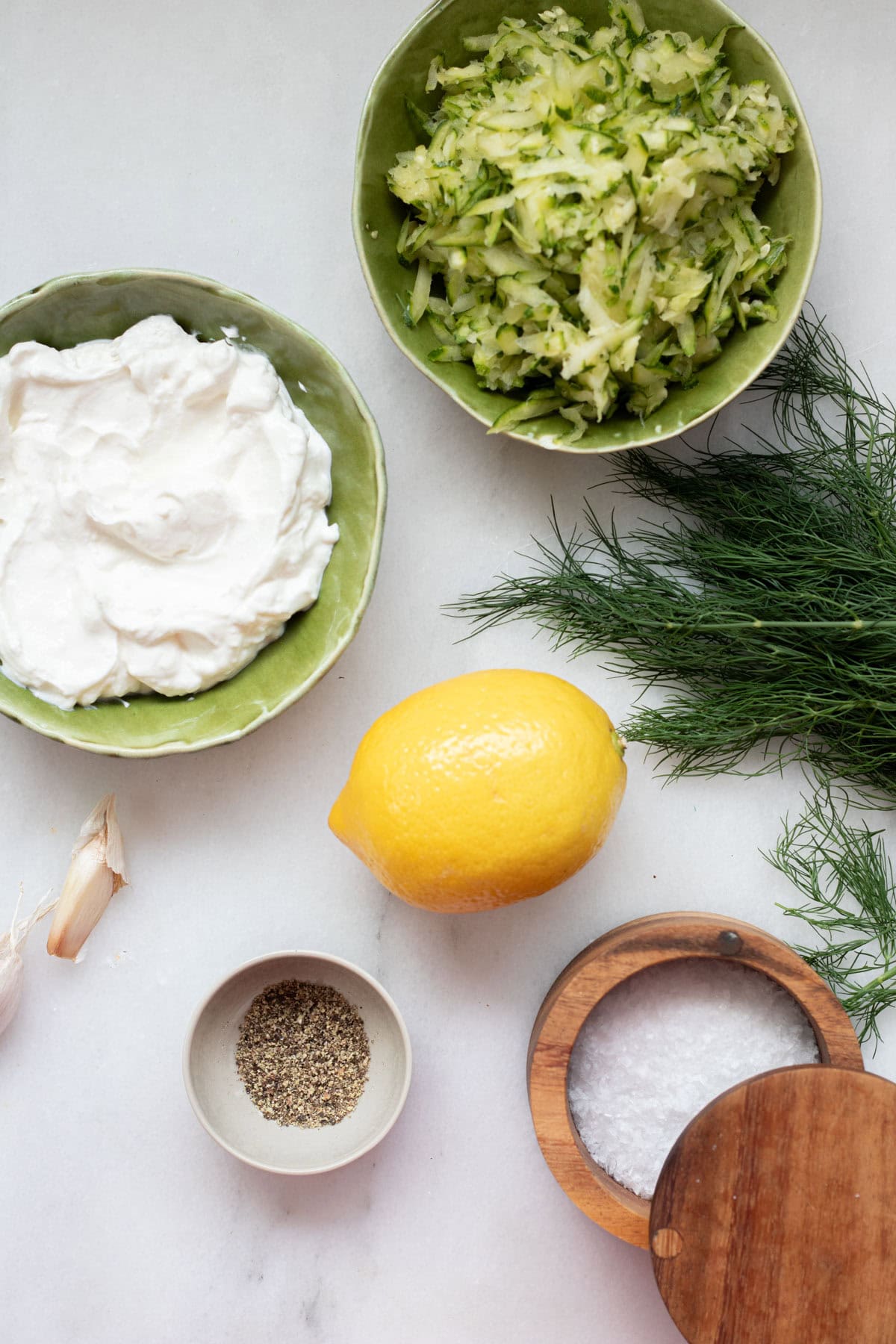 ingredients for zucchini tzatziki in small bowls on white background