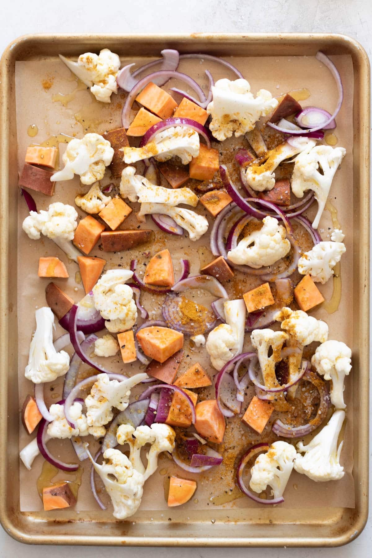 veggies ready for roasting on a sheet tray, cauliflower, sweet potato, and red onion