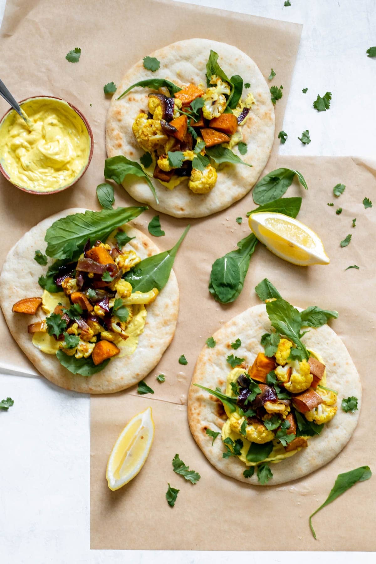 pita lying flat on parchment paper topped wtih veggies