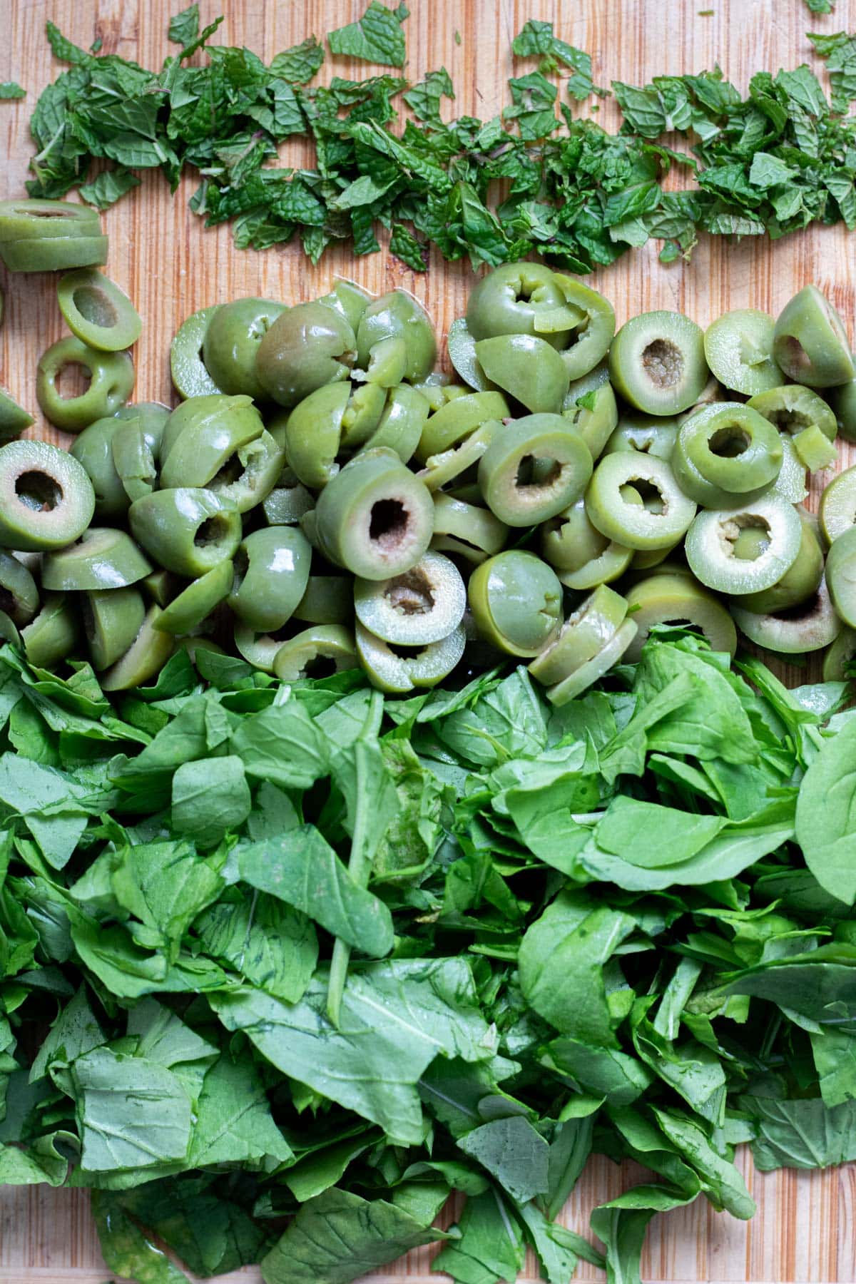 chopped mint, olives and arugula on a brown cutting board