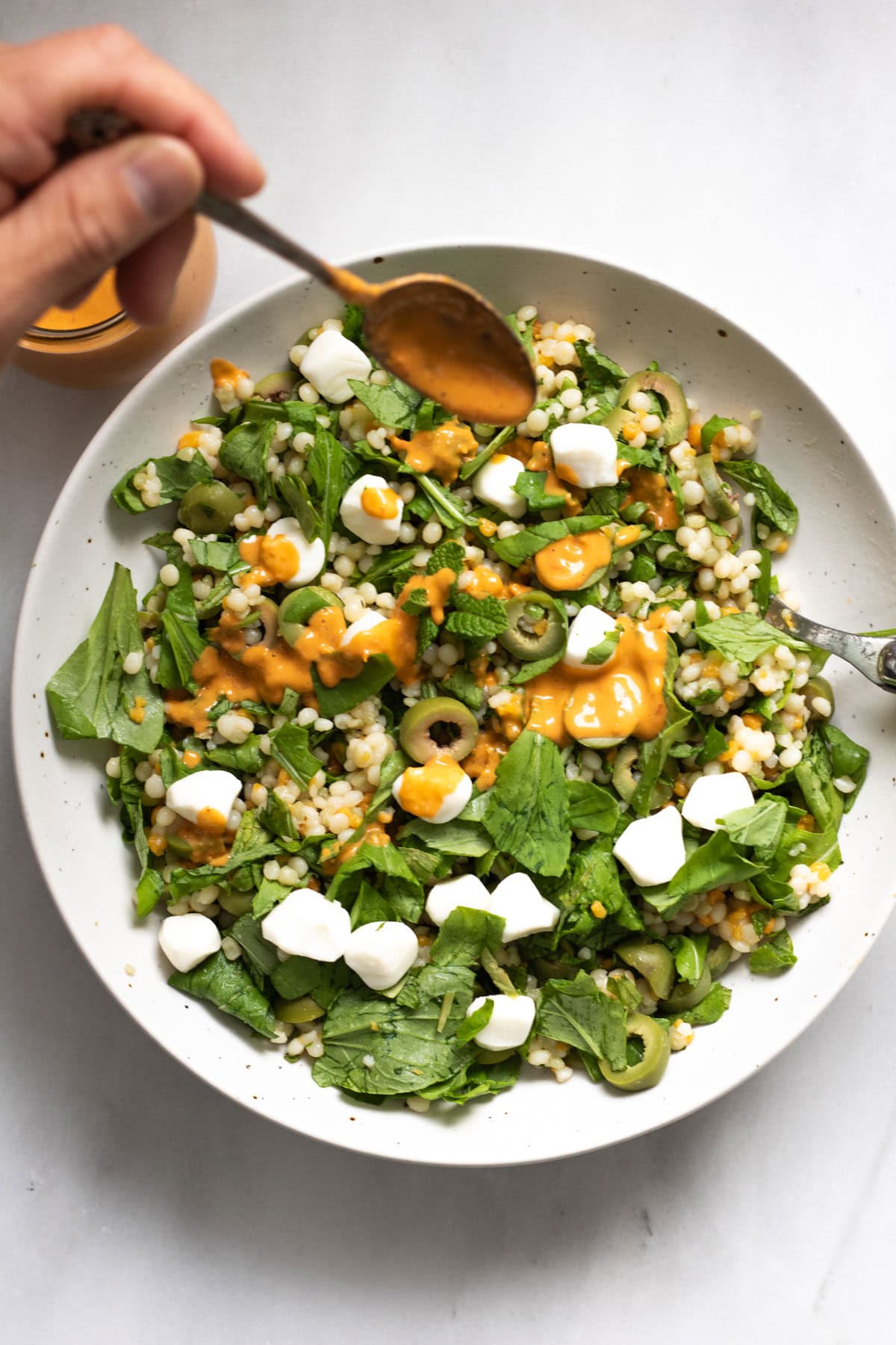 Olive CousCous Salad with tomato vineigrette in a white bowl