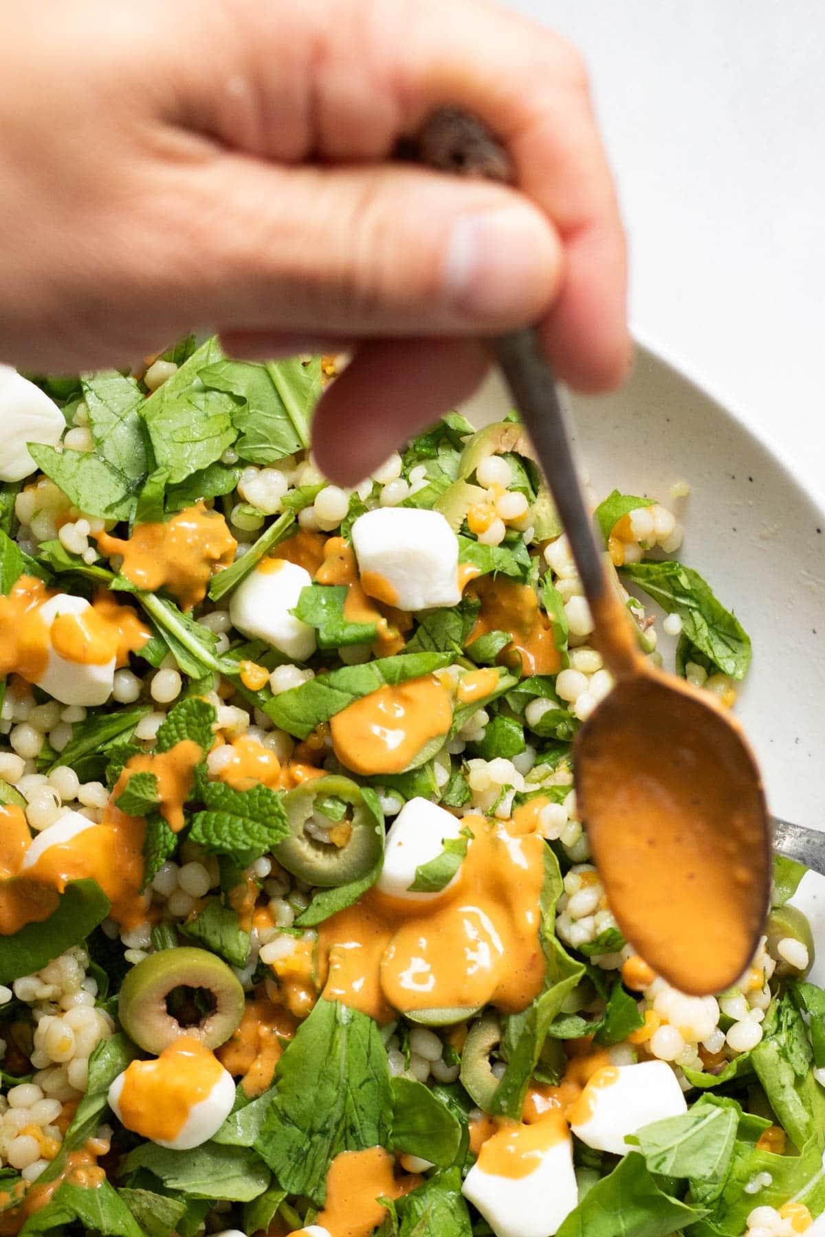 drizzling tomato vineigrette on a bowl of olive couscous salad