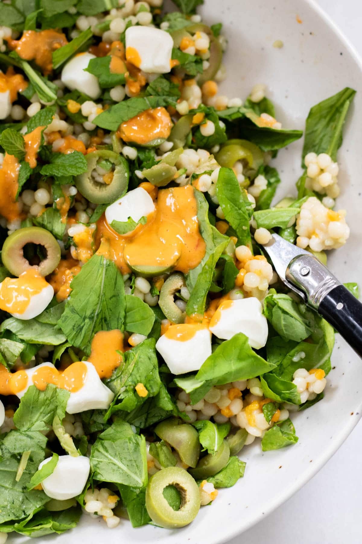 Olive CousCous Salad with tomato vineigrette in a white bowl