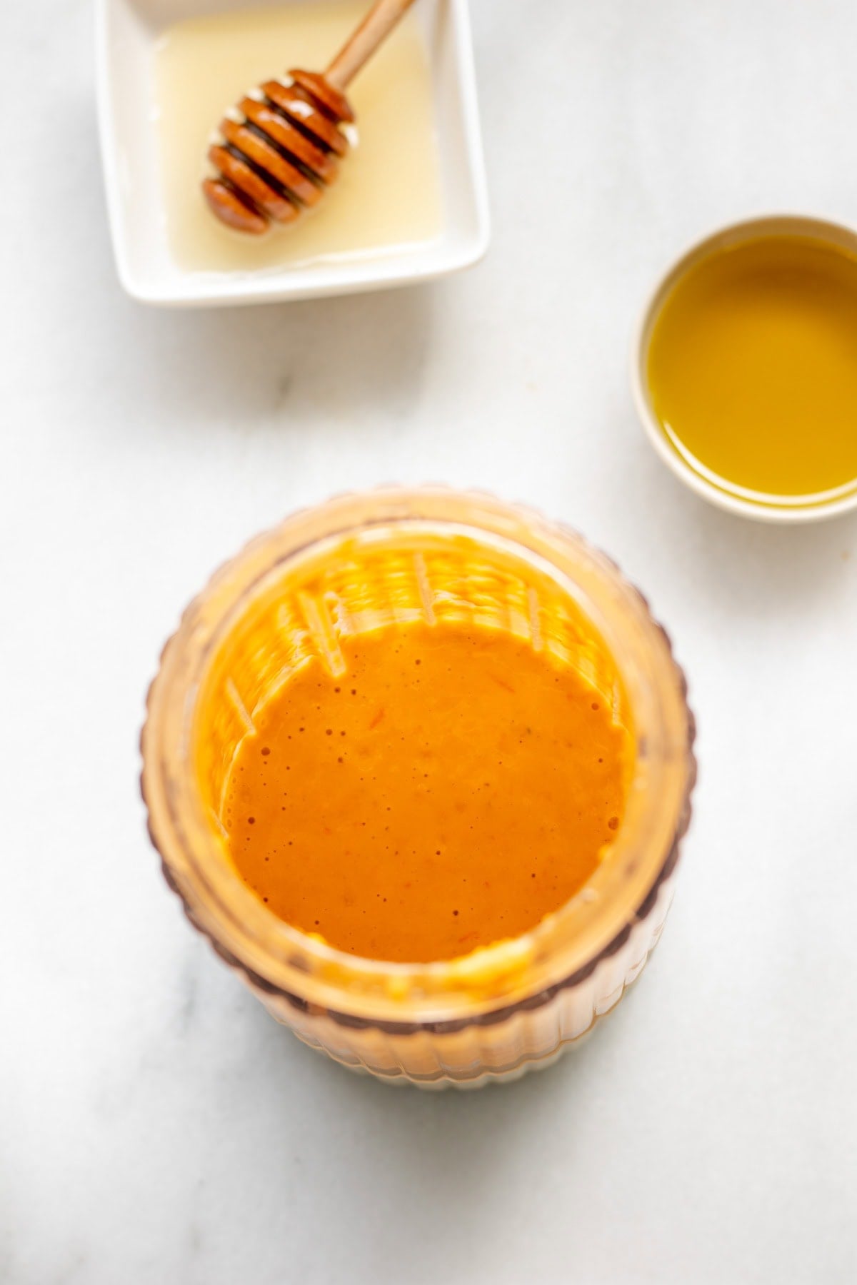 tomato vinaigrette in a blender cup next to a small bowl of honey