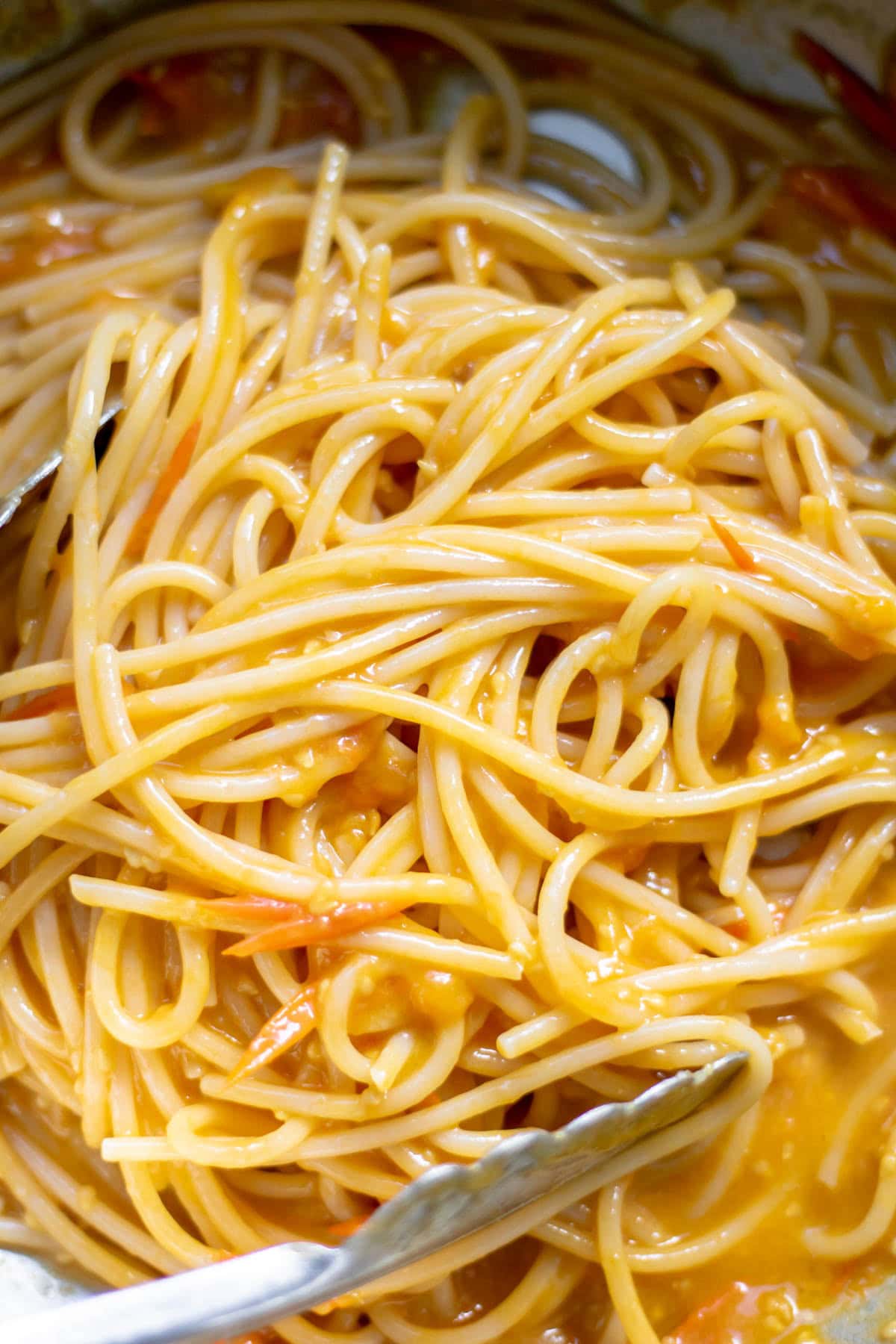tongs in a pot of pasta with sungold tomato sauce