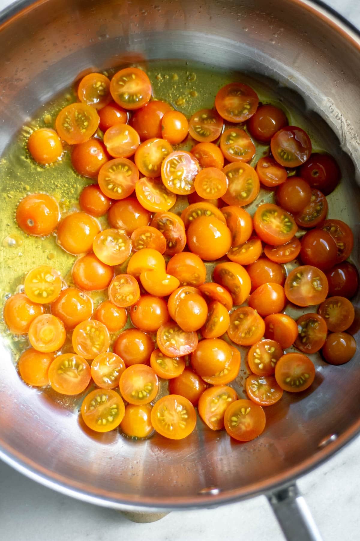 adding fresh sungold tomatoes to a pan with olive oil and salt