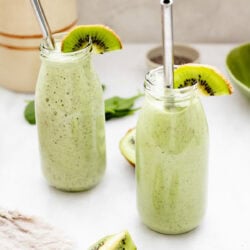two glasses of tropical kiwi smoothie with metal straws on white background
