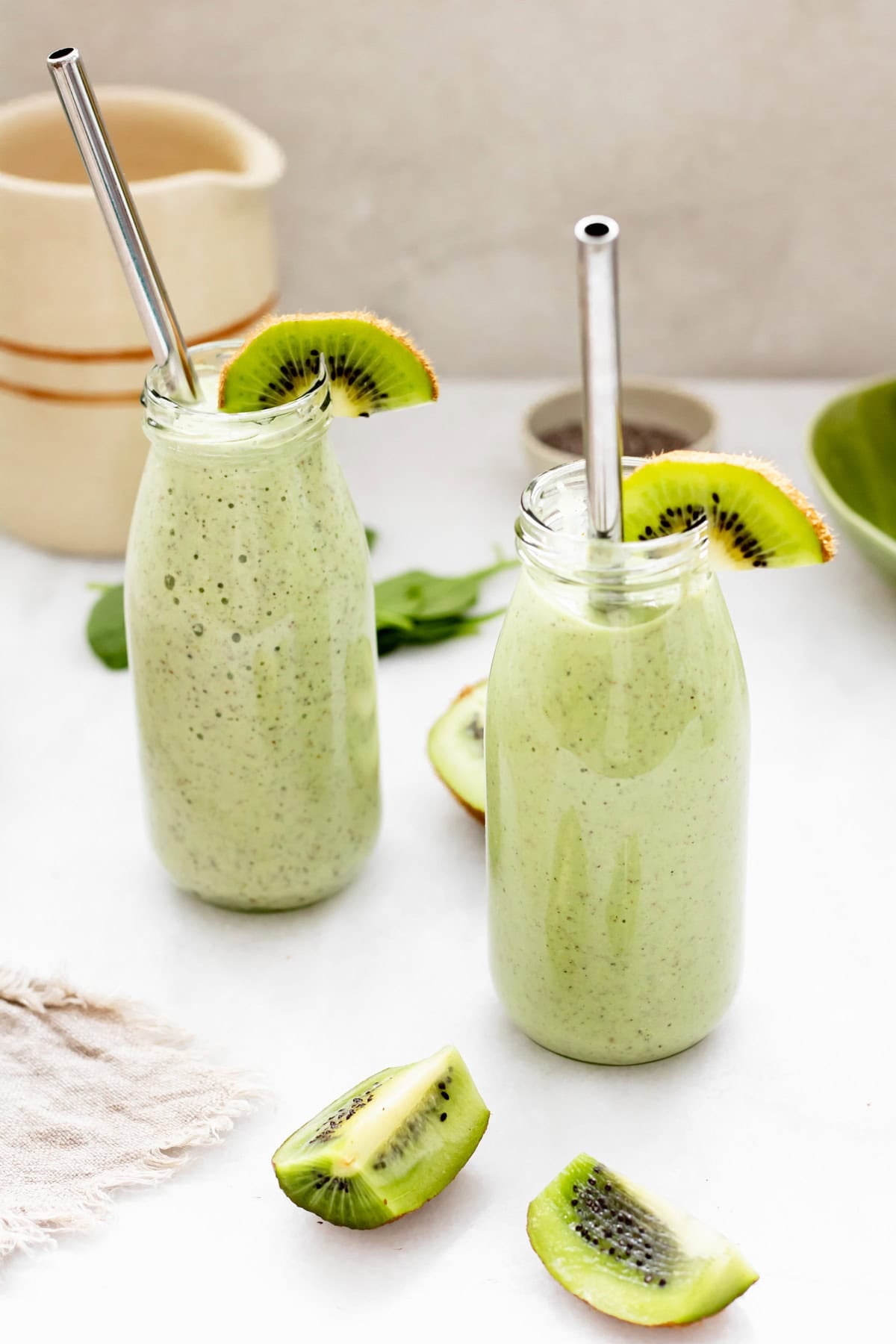 two glasses of tropical kiwi smoothie with metal straws on white background