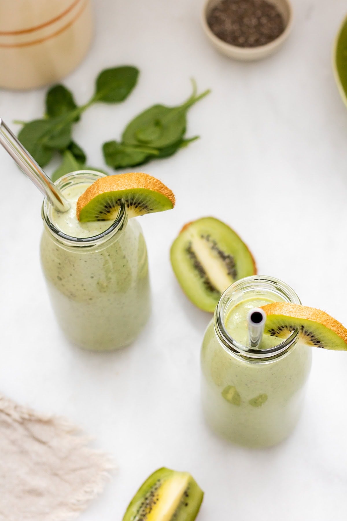 two glasses of tropical kiwi smoothie with metal straws on white background