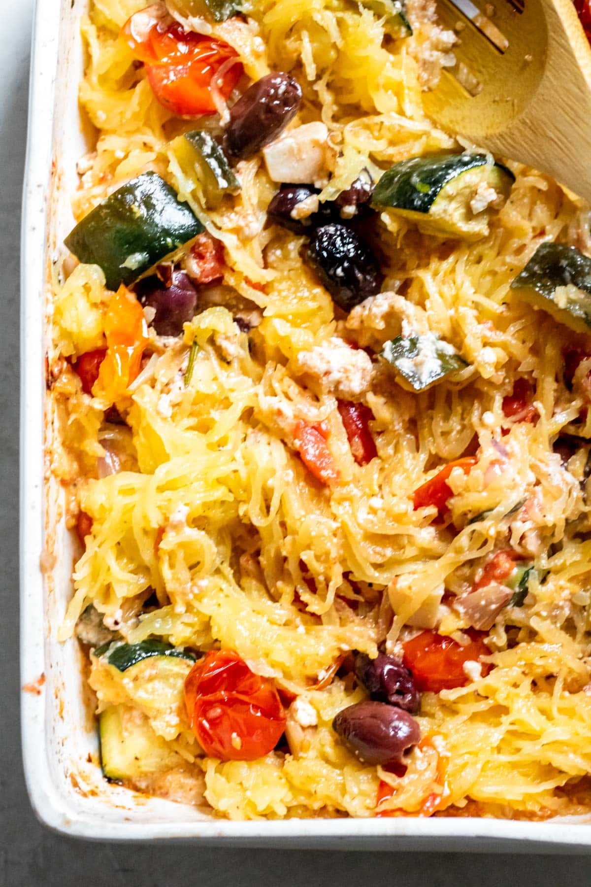 mixing spaghetti squash, baked feta and veggies together in a baking dish