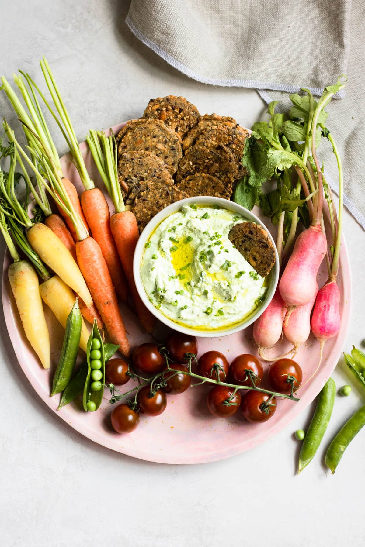 charcuterie board with fresh carrots, cherry tomatoes, peas, crackers and green dip