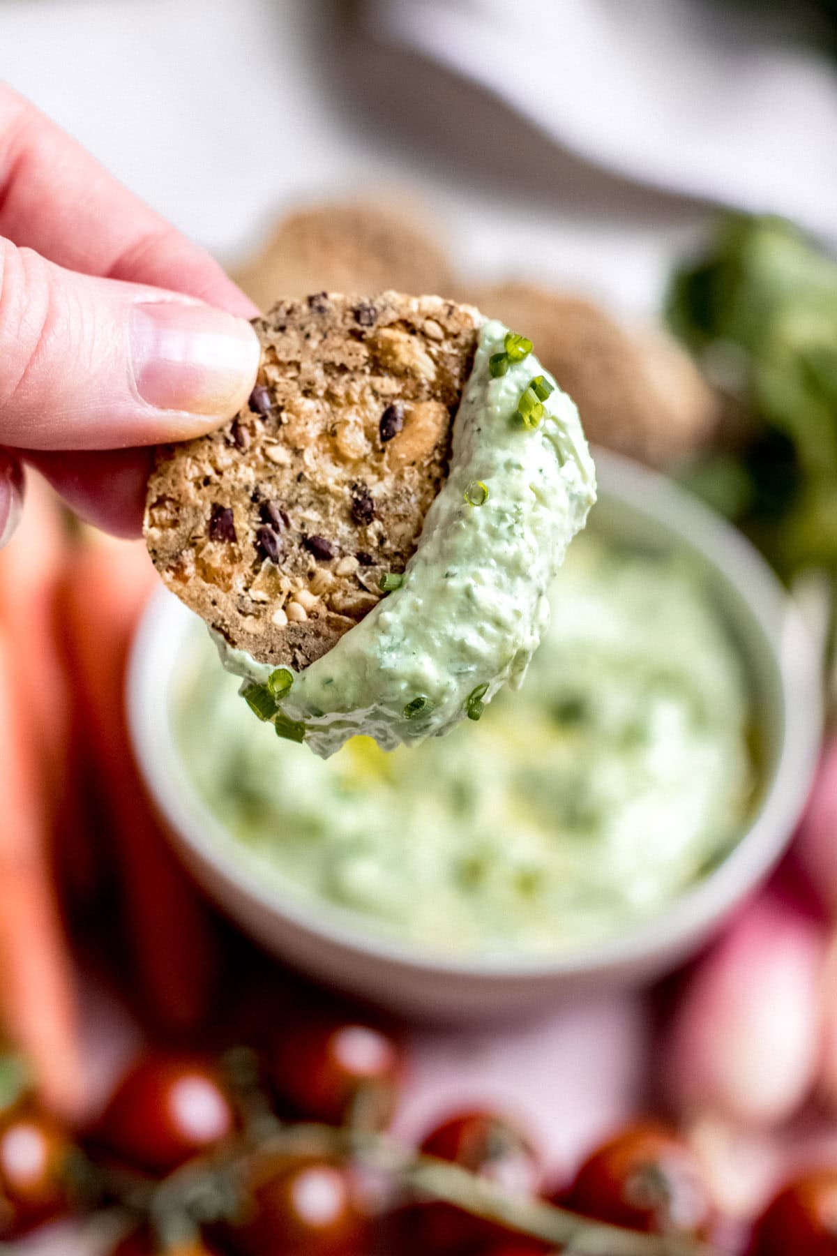 hand dipping cracker into green goddess ricotta dip