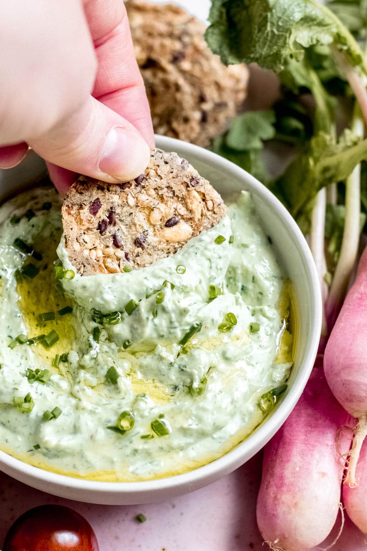 hand dipping cracker into green goddess ricotta dip