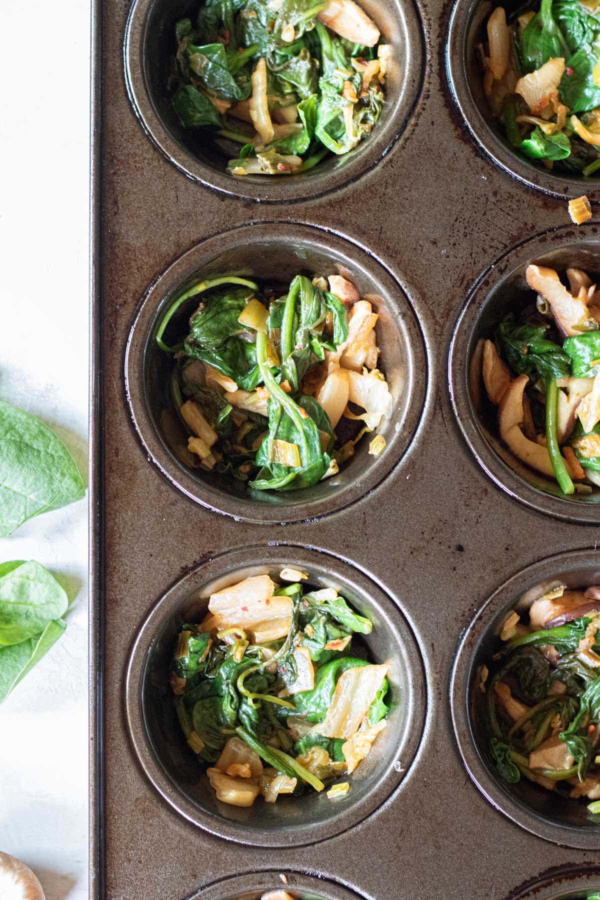 scallion-mushroom-spinach-kimchi mix put in the bottom of each slot of a muffin tin