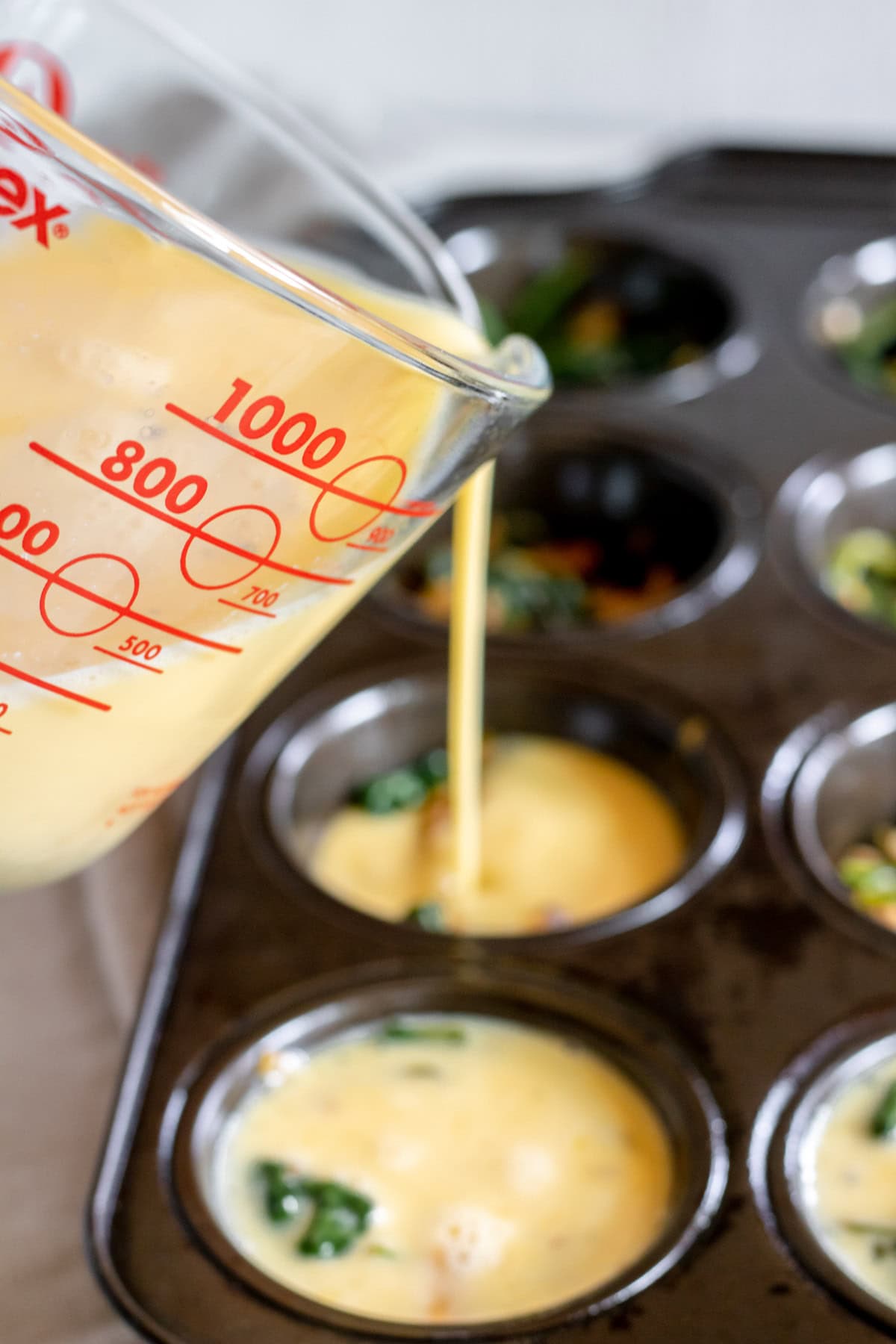 pouring egg mixture on top of scallion-mushroom-spinach-kimchi mix in each slot of a muffin tin