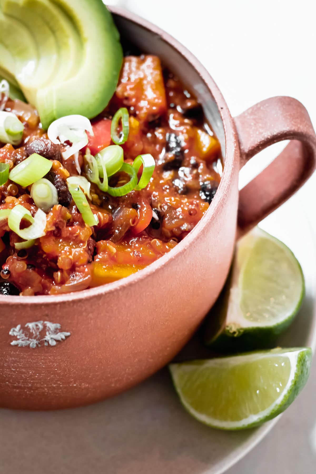 close up of Healthy Quinoa Butternut Squash Chili with avocado slices in a red soup bowl