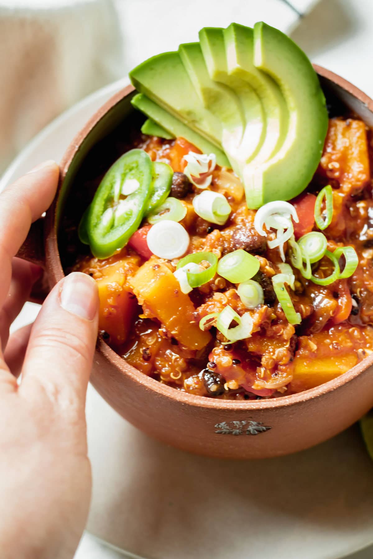 Healthy Quinoa Butternut Squash Chili with avocado slices in a red soup bowl