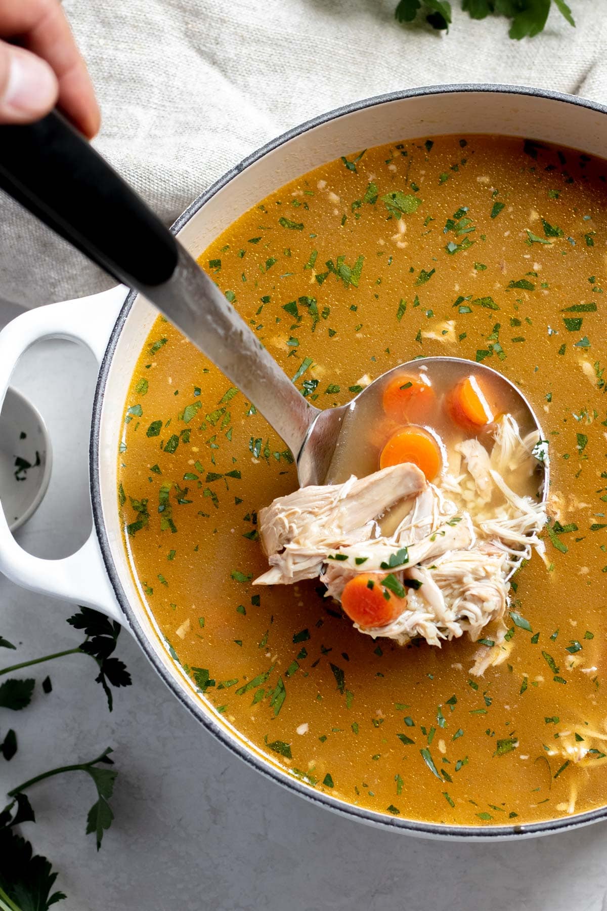 ladle full of chicken noodle soup in a large white pot