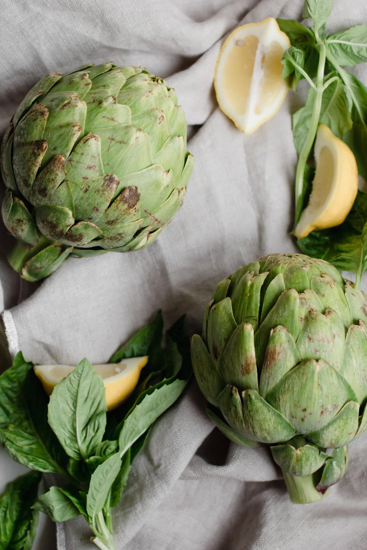 raw artichokes, lemon slices and basil on a cloth
