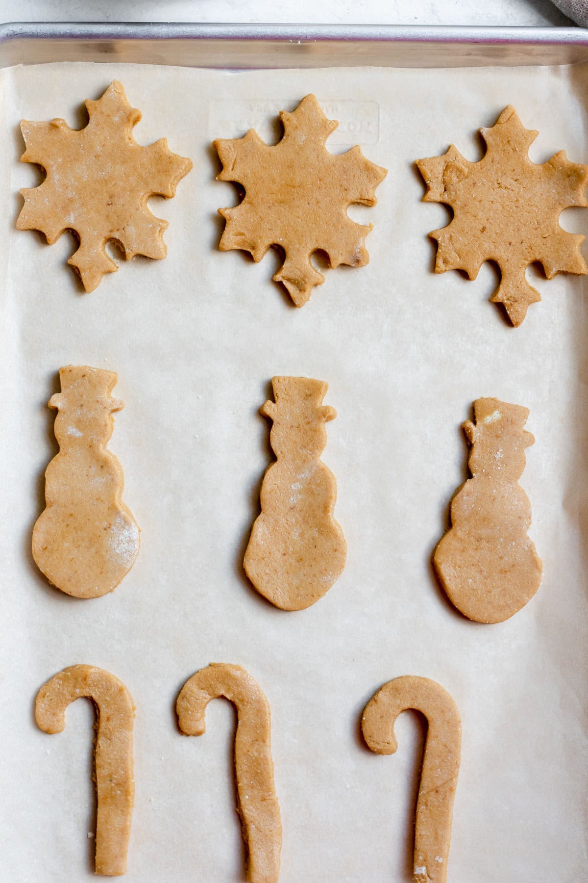 snowflake, snowman and candy cane shaped cookie dough cutouts on a baking tray