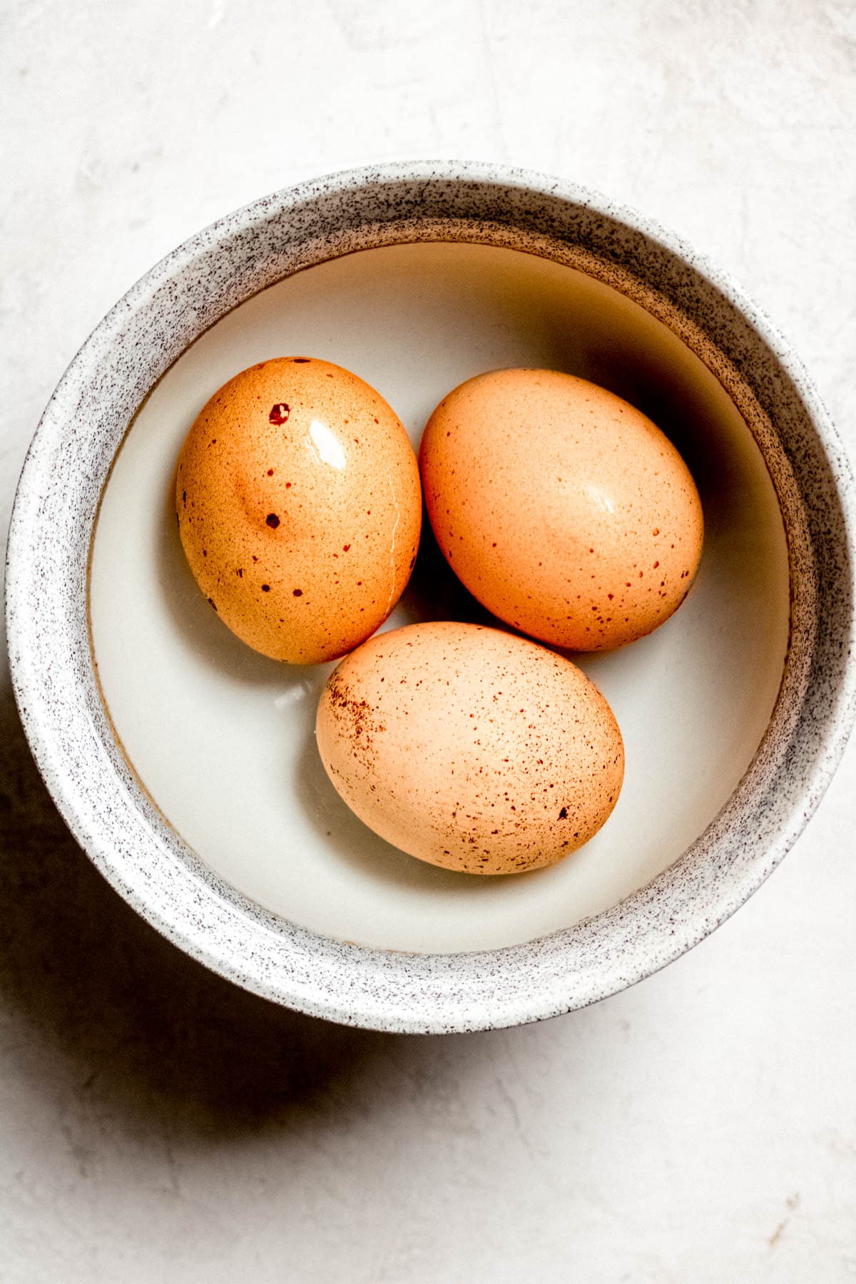 three boiled eggs with the shells on in a small bowl