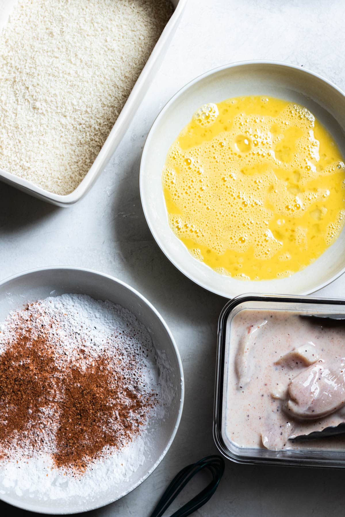 breadcrumbs, dry ingredients, wet ingredients and marinated chicken on a table