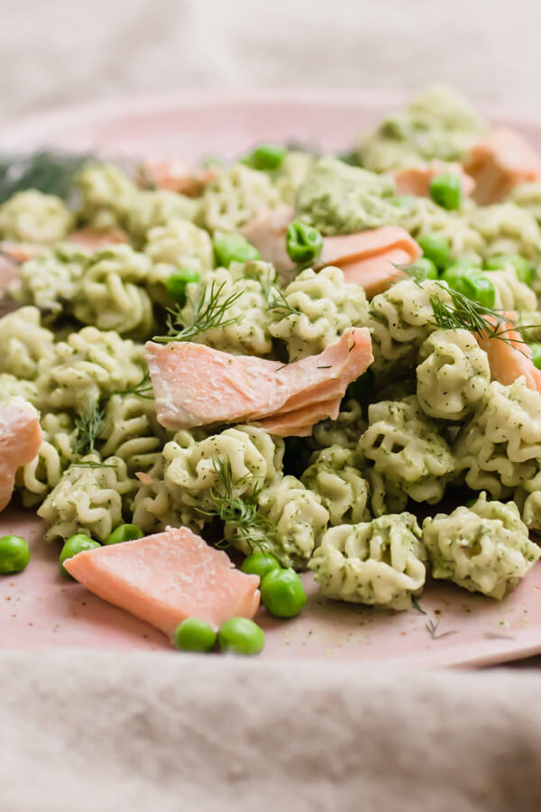 Pesto pasta with peas and poached salmon on a pink plate