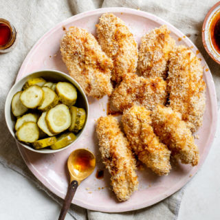 pink plate of HEALTHIER! Crispy Baked Nashville Hot Chicken Strips (Buttermilk Marinated!) with a bowl of pickles