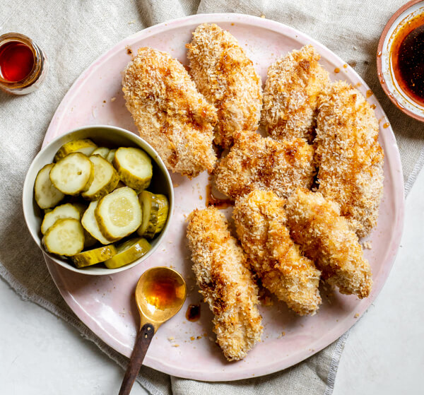 pink plate of HEALTHIER! Crispy Baked Nashville Hot Chicken Strips (Buttermilk Marinated!) with a bowl of pickles