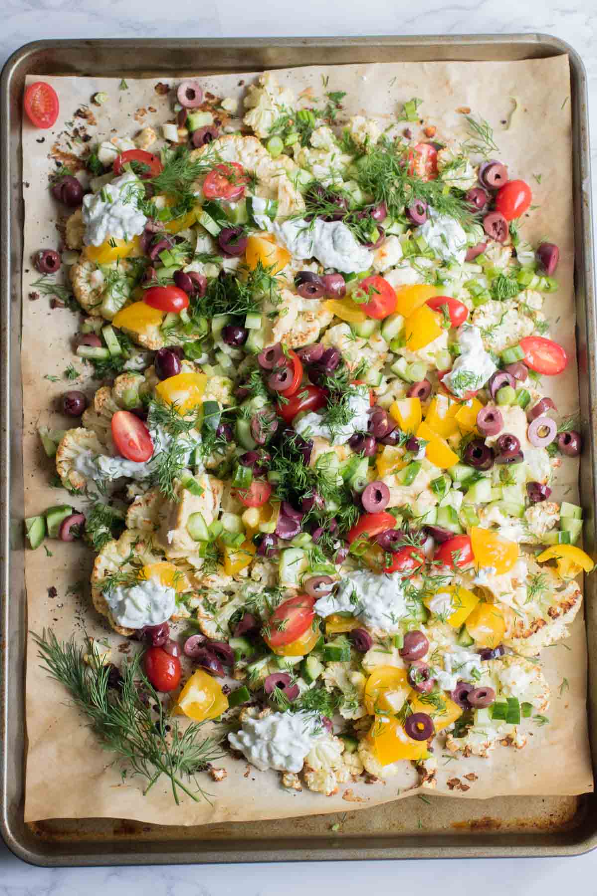 Loaded Mediterranean Cauliflower Nachos are piled high with creamy feta cheese, crunchy cucumbers, hummus, olives, tzatziki sauce and more! So delicious you won't want to share. | abraskitchen.com