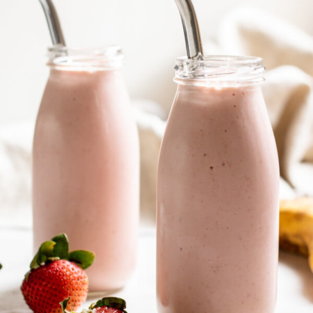 Strawberry Banana Adaptogen Smoothie in two glass jars with straws on white background