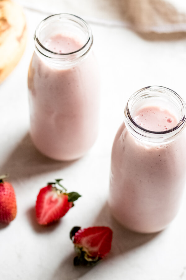 Strawberry Banana Adaptogen Smoothie in 2 glass bottles on white background with strawberries